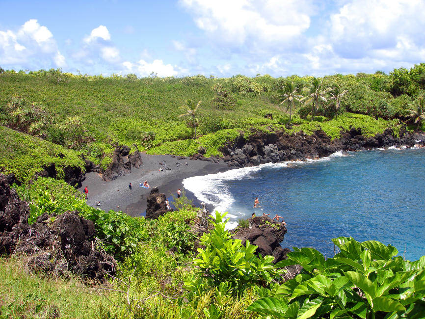 A black sand beach surrounded by green foliage on my maui winter packing list post